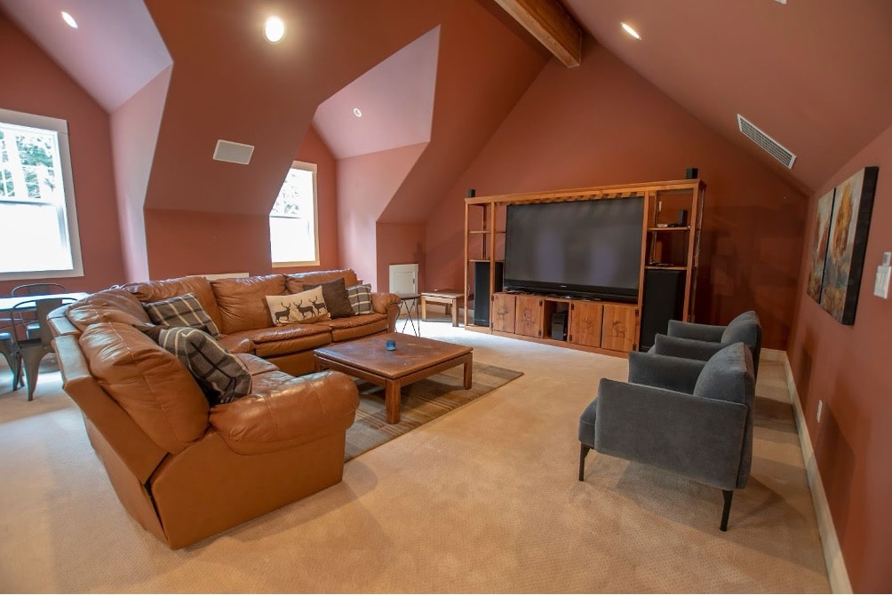 Spacious living room with vaulted ceilings, tan leather sectional, entertainment center, and warm terracotta walls.