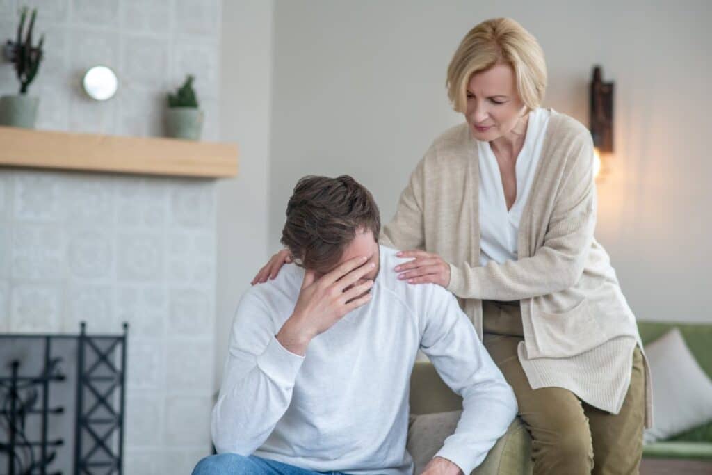mother supporting her son who is sitting with his hand on his head, illustrating how to help a loved one with depression