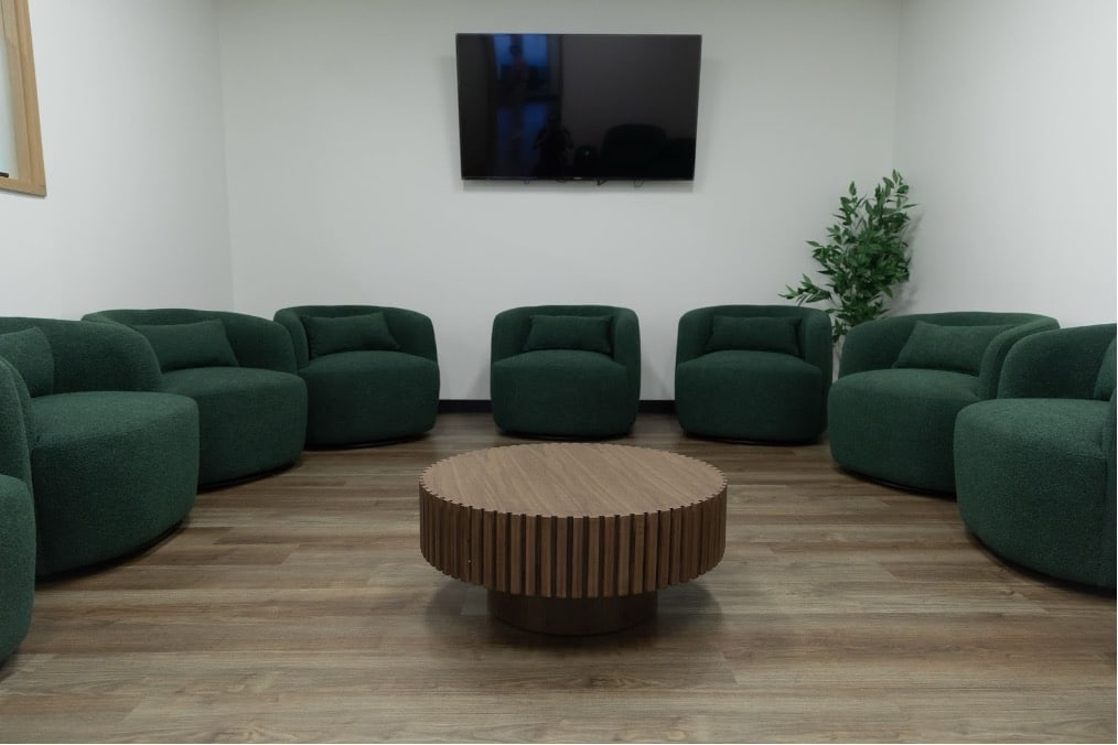 Modern therapy waiting room with circular arrangement of deep green seating, wooden coffee table, and minimalist decor.