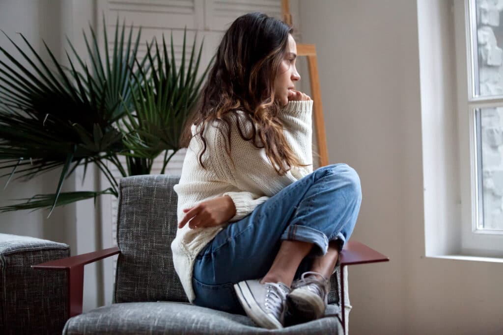 woman sitting in chair, gazing out the window, wondering about bipolar 1 and 2 differences