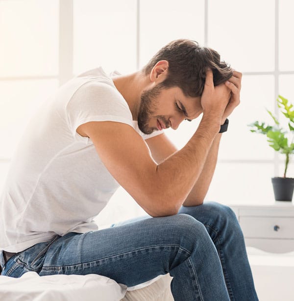 man anxious sitting on bed hands on head