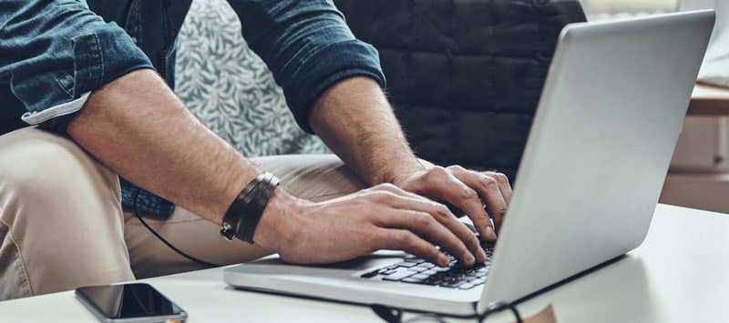 man sitting on couch typing on computer