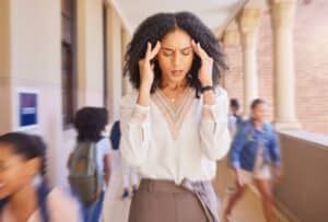 Female teacher standing in hallway holding hands on temples of her head with her eyes closed
