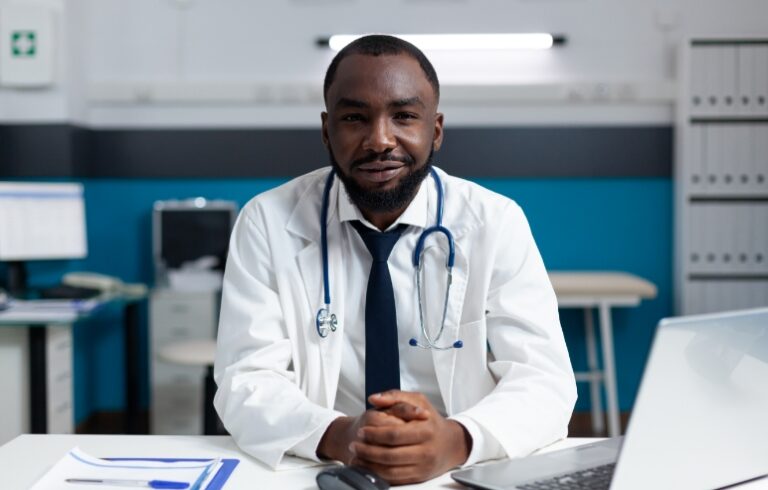 Male doctor sitting at desk with white coat and stethoscope on