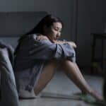 depressed woman sitting on bedroom floor in need of a stay at short term mental health facilities