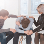 a man experiencing grief crying into arms while his family supports him with hands on his back