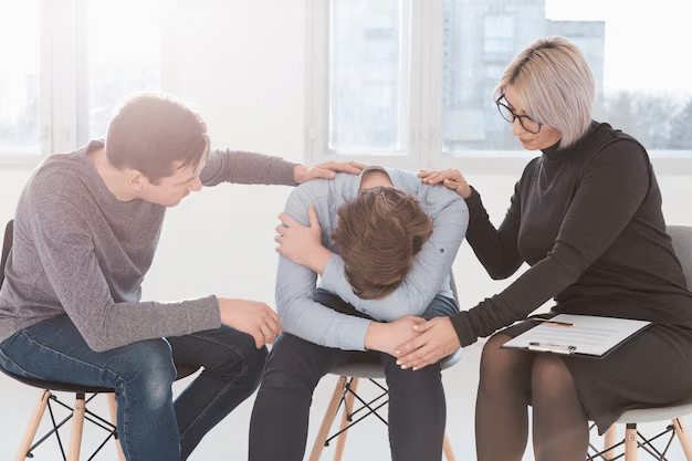 a man experiencing grief crying into arms while his family supports him with hands on his back