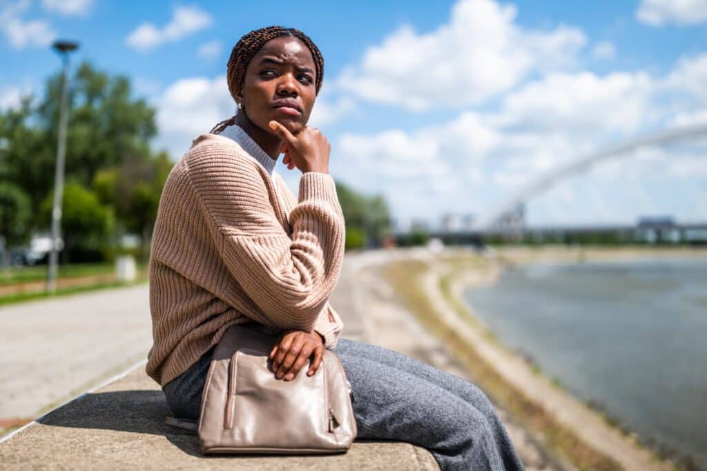 woman outdoors, sitting on concrete wall, looking pensive and contemplating, "Is major depressive disorder the same as depression?"