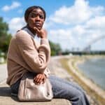 woman outdoors, sitting on concrete wall, looking pensive and contemplating, "Is major depressive disorder the same as depression?"