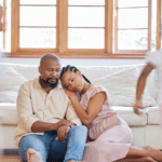 parents sitting on the floor, looking tired and worried while kids run around them, wondering, "Is anxiety genetic?"