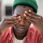 man with green hat covering his eyes with his hands, experiencing free floating anxiety