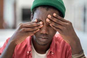 man with green hat covering his eyes with his hands, experiencing free-floating anxiety