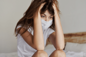 woman with hands on head and facemask on, wondering, "Is anxiety contagious?"