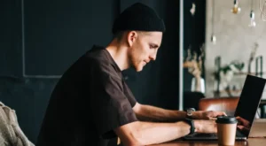 Young man wearing a beanie sitting at a desk researching on his laptop