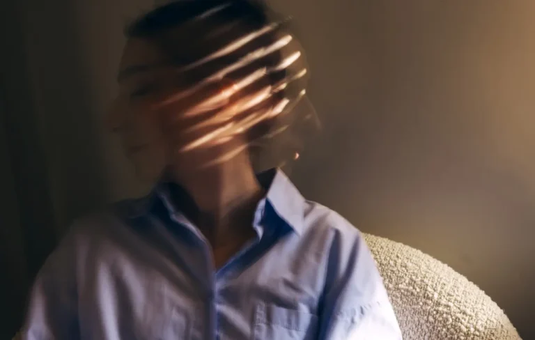 woman in collared shirt sitting in a chair with window lighting across her face, contemplating the different types of schizophrenia and what she may be experiencing
