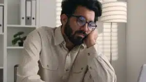 Man with beard and glasses holding his face in his hands from burnout