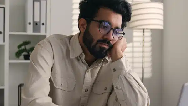 Man with beard and glasses holding his face in his hands from burnout