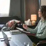 Woman sitting at desk wondering, "Why would I want to relive traumatic memories in therapy?"