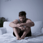 Man sitting on his bed looking down in need of mental health treatment