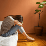Woman sitting on the edge of her bed with her head in her hands due to self-sabotaging behaviors