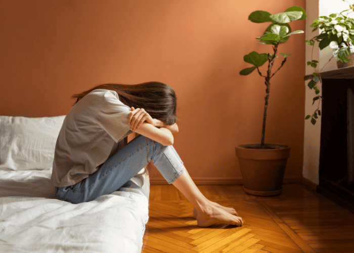 Woman sitting on the edge of her bed with her head in her hands due to self-sabotaging behaviors