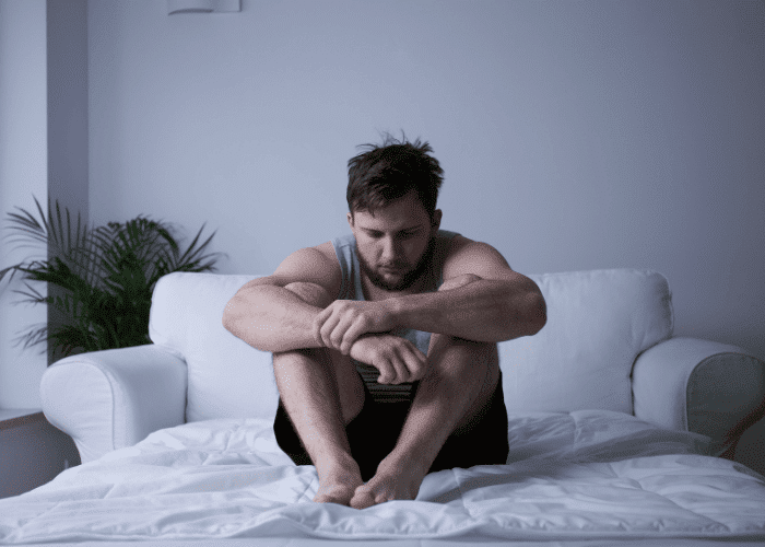 Man sitting on his bed looking down in need of mental health treatment