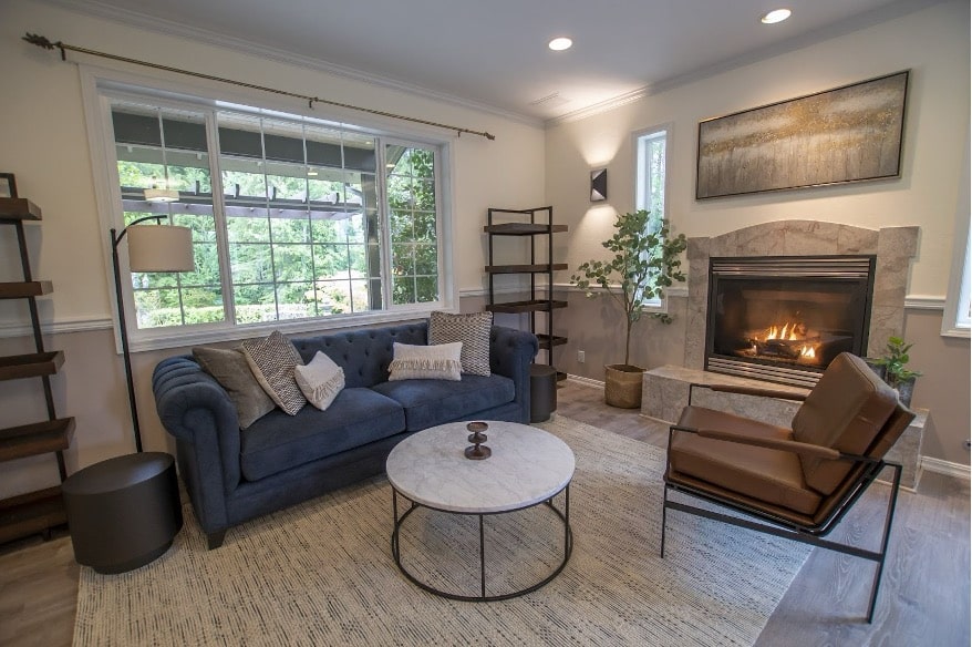 Mission Prep modern living room with navy blue tufted sofa, leather accent chair, round coffee table, and stone fireplace with flames.