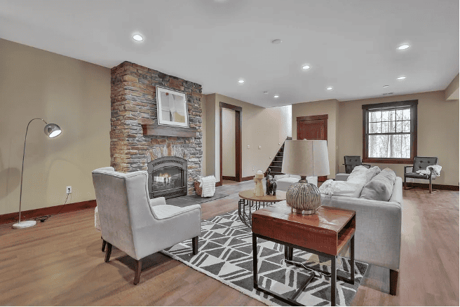 Modern living room with stone fireplace, gray upholstered furniture, hardwood flooring, and geometric area rug.