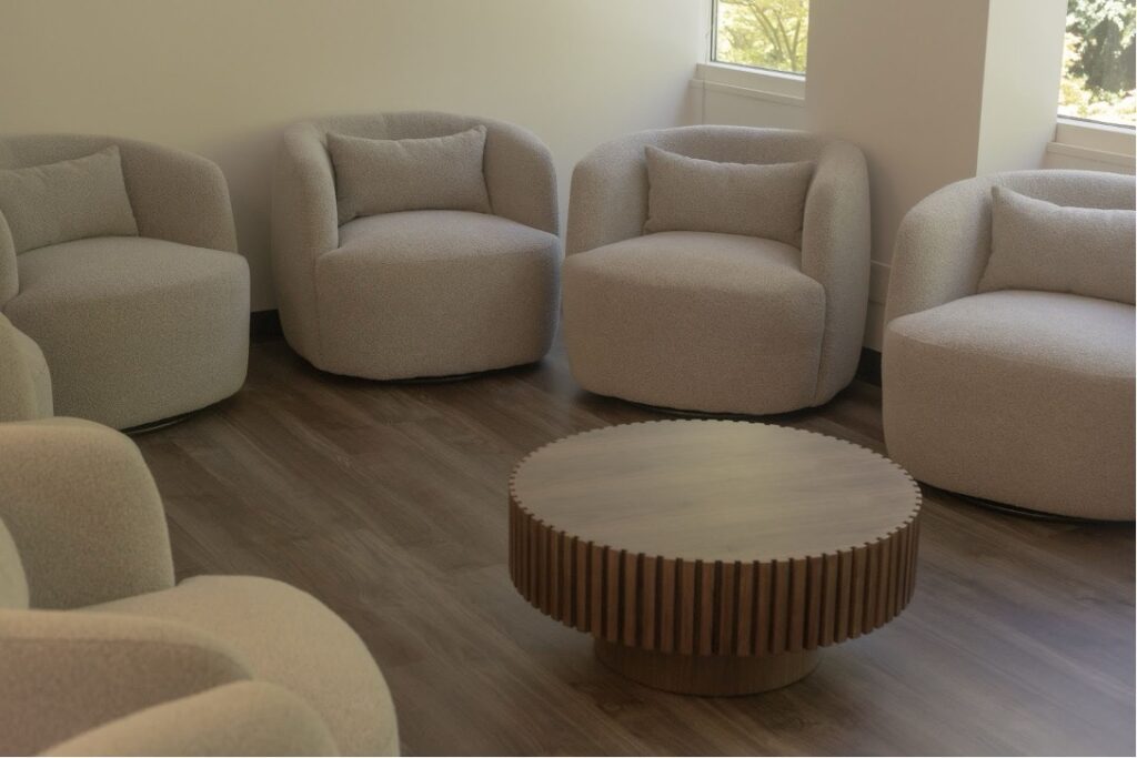 Modern therapy waiting room with rounded beige chairs arranged in a circle around a wooden coffee table.