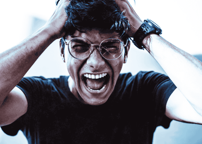 Man with broken glasses screaming with his hands on his head due to acute stress disorder