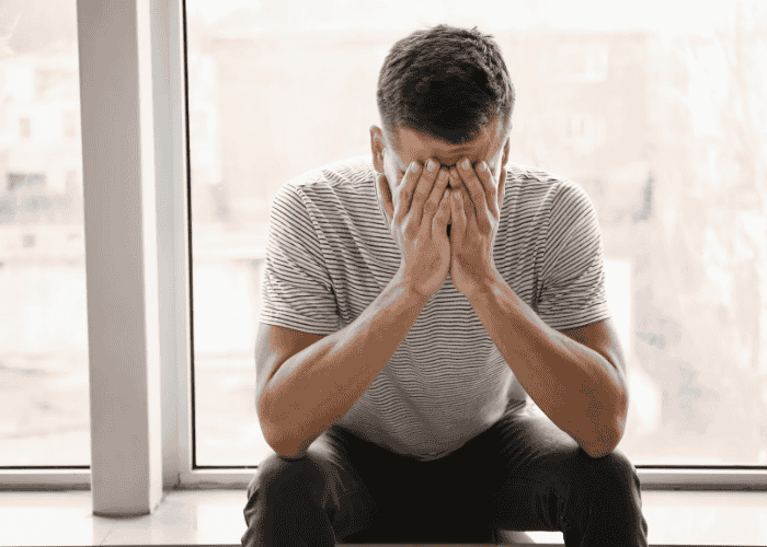 Man sitting on a window ledge with his head in his hands, asking is depression genetic?