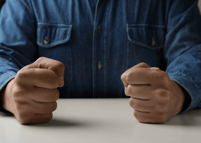 Man sitting at a table with his fists clenched on the table, in need of chronic anger & conduct disorder treatment