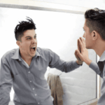 Man with straight face looking in the mirror, which shows himself shouting back, in need of bipolar disorder treatment