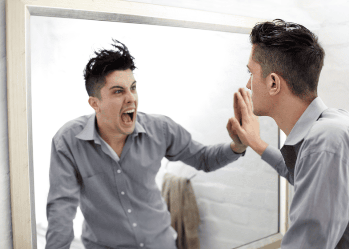 Man with straight face looking in the mirror, which shows himself shouting back, in need of bipolar disorder treatment