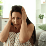 Woman sitting on the floor with her knees to her chest, her hands over her ears, with a panicked expression, in need of psychosis treatment