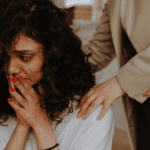 Woman facing forwards with her hands on her face, looking traumatized and in need of trauma treatment