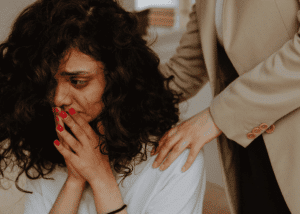 Woman facing forwards with her hands on her face, looking traumatized and in need of trauma treatment