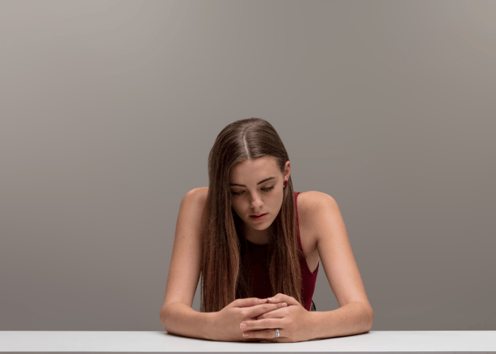 Woman sitting with her arms on the table looking down at her arms, in need of self-harm treatment