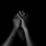 Man sitting on his own in the dark with his hands over his face, in need of existential depression treatment