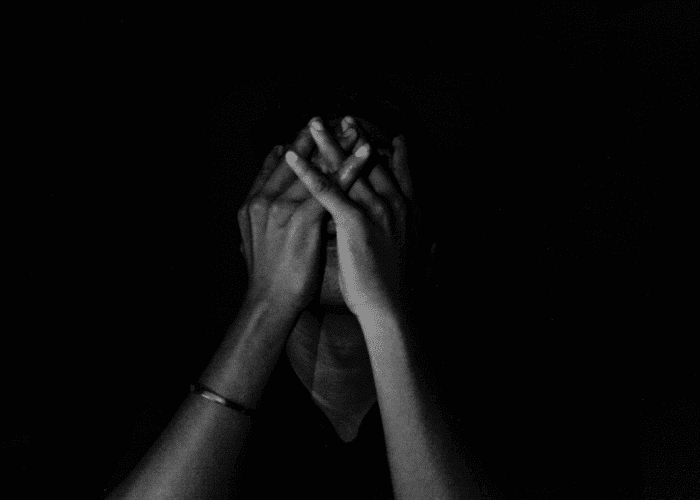 Man sitting on his own in the dark with his hands over his face, in need of existential depression treatment