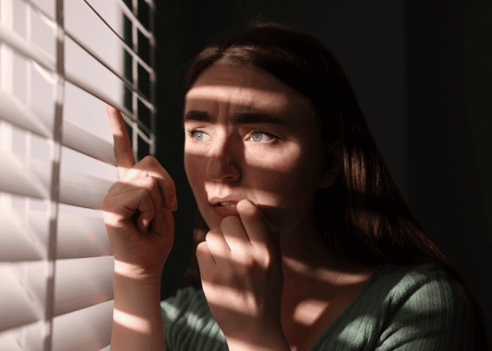 Woman looking out the window feeling paranoid in need of schizophrenia treatment