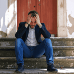 Man sitting outdoors on steps with his head in his hands, looking distraught due to antisocial personality disorder in adults