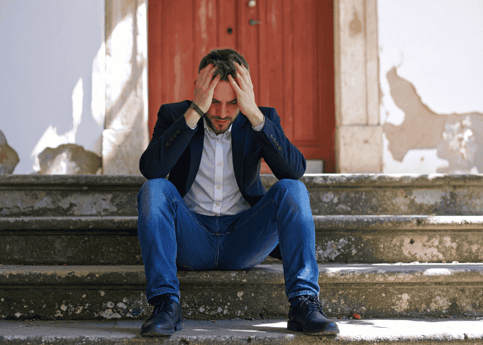 Man sitting outdoors on steps with his head in his hands, looking distraught due to antisocial personality disorder in adults