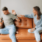 Couple sitting on the sofa, man with his hand out stopping his girlfriend from coming close due to avoidant personality disorder in adults