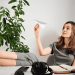 woman sitting at her desk throwing a paper aeroplane wondering, "Is procrastination a sign of depression?"