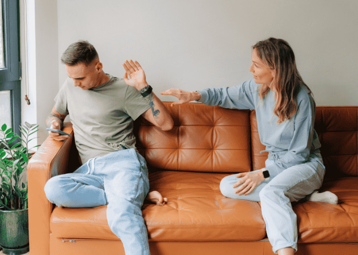 Couple sitting on the sofa, man with his hand out stopping his girlfriend from coming close due to avoidant personality disorder in adults