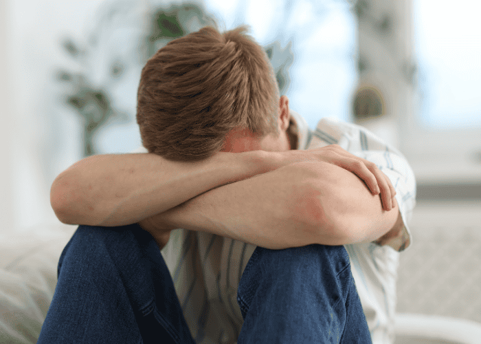 Man with his knees to his chest and his head and arms over his legs experiencing common anxiety symptoms in adults