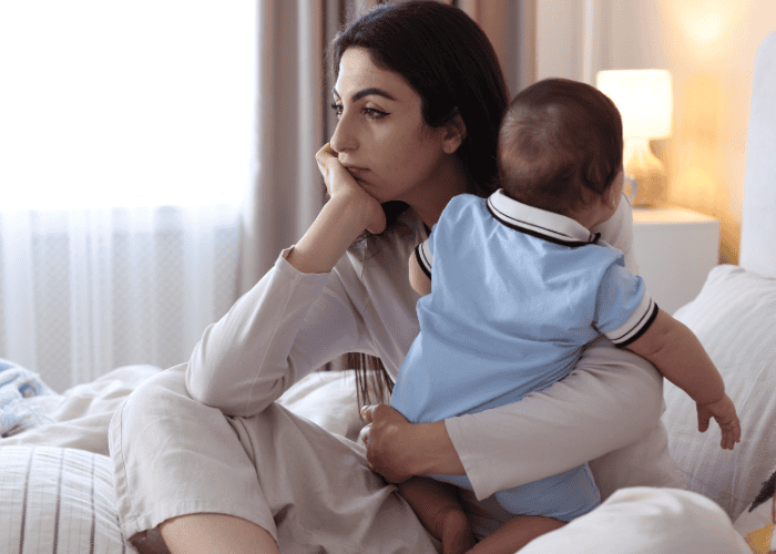 Woman holding baby looking out of the window struggling with social anxiety and depression