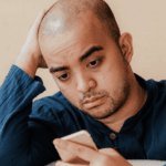 Man looking worriedly at his phone, struggling with adult separation anxiety disorder