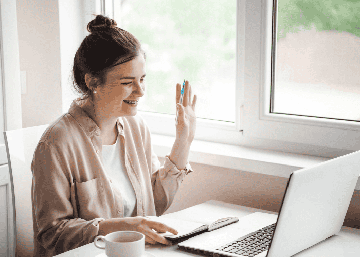 Woman sitting with her laptop open waving and smiling as she tries online therapy for bipolar disorder